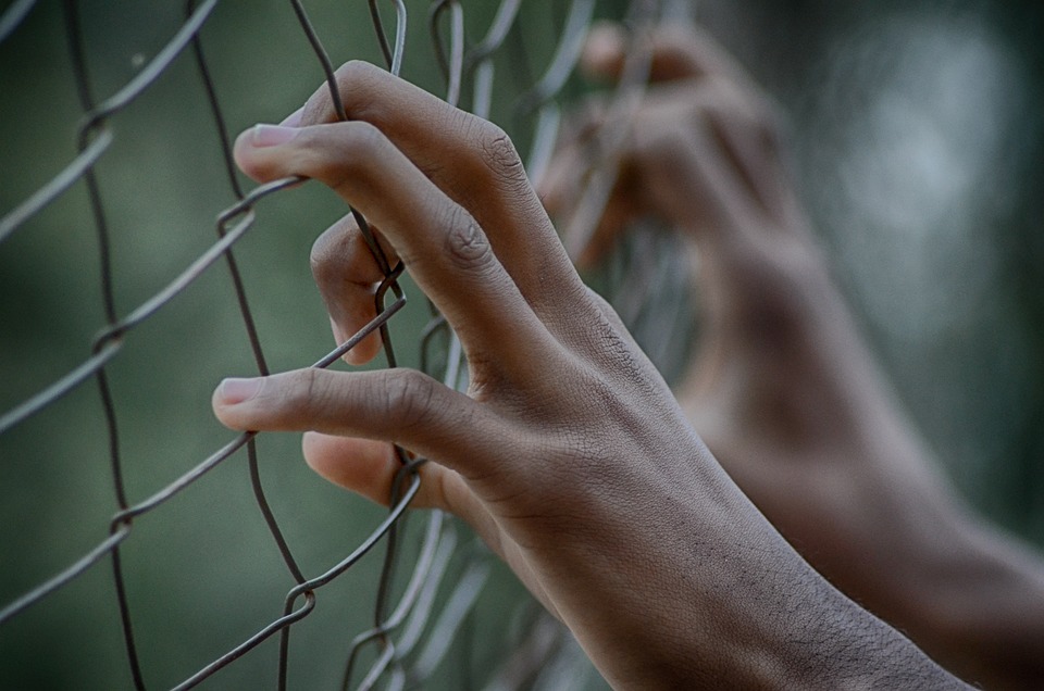 mani dietro ad una recinzione